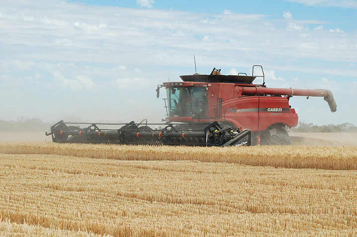 Wind is blowing dust and debris behind a harvester machine, not in front, as it travels into the wind.